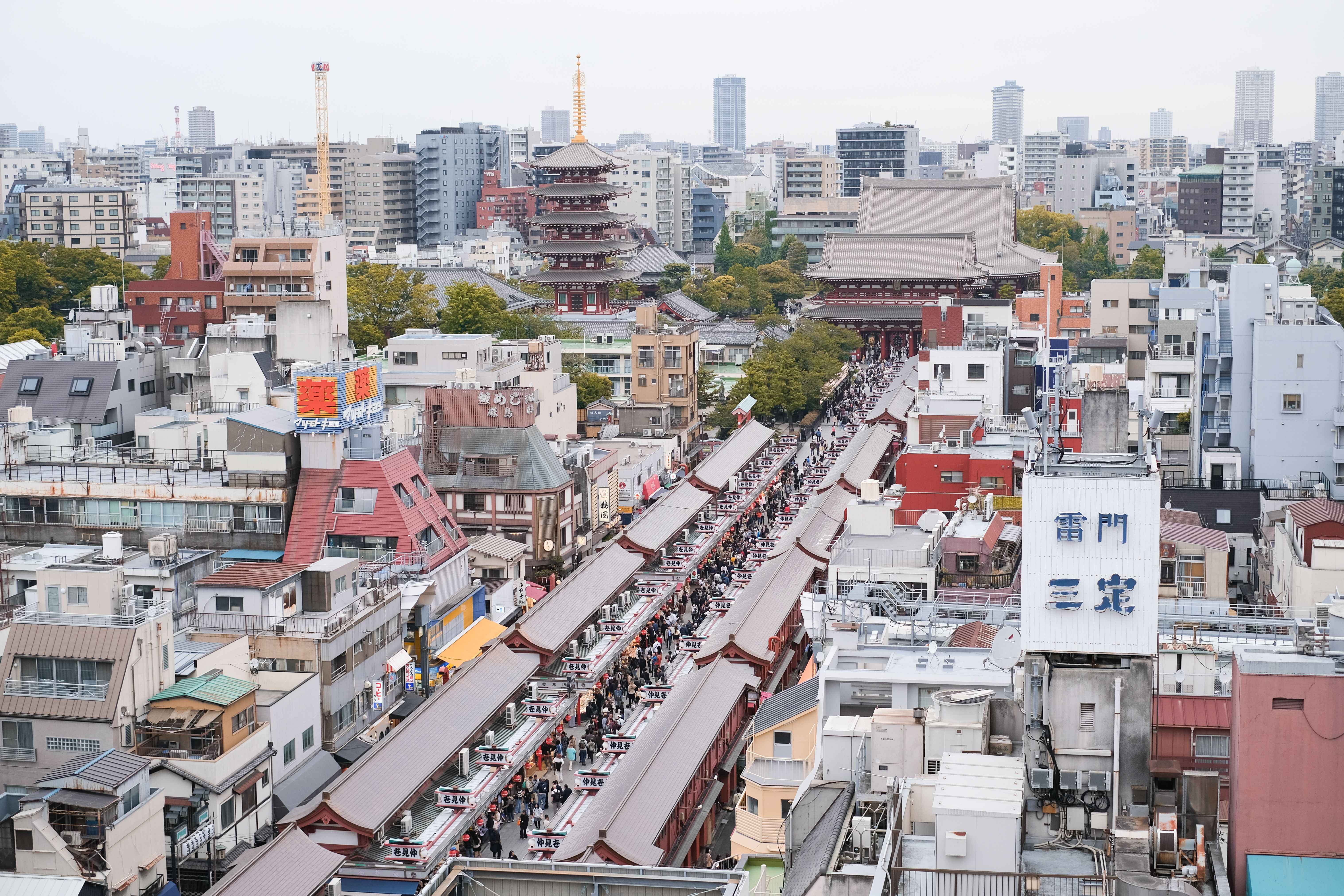 Bustling street scene leading to the historic Senso-ji Temple surrounded by a cityscape in Tokyo.