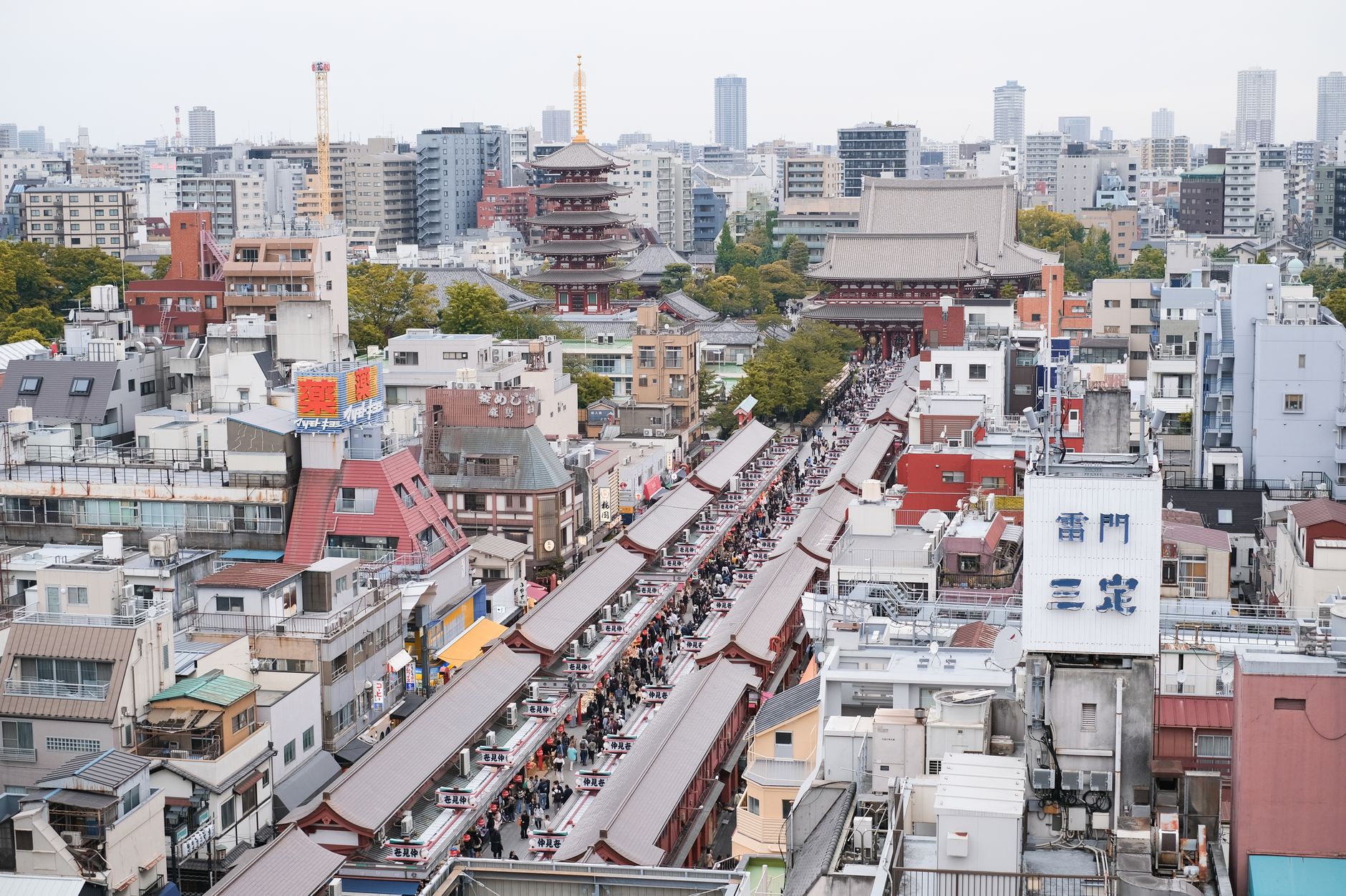 Bustling street scene leading to the historic Senso-ji Temple surrounded by a cityscape in Tokyo.