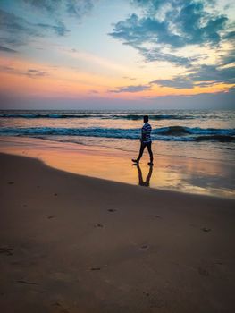 A lone figure walks along a serene beach at sunset, enjoying the vivid hues of the sky and the tranquil waves.