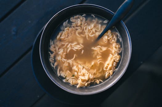 A close-up view of a warm bowl of instant ramen noodles with broth on a dark surface.
