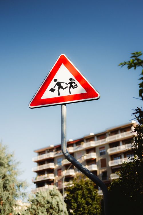 Free Red triangular warning sign for school zone in urban area against clear blue sky. Stock Photo