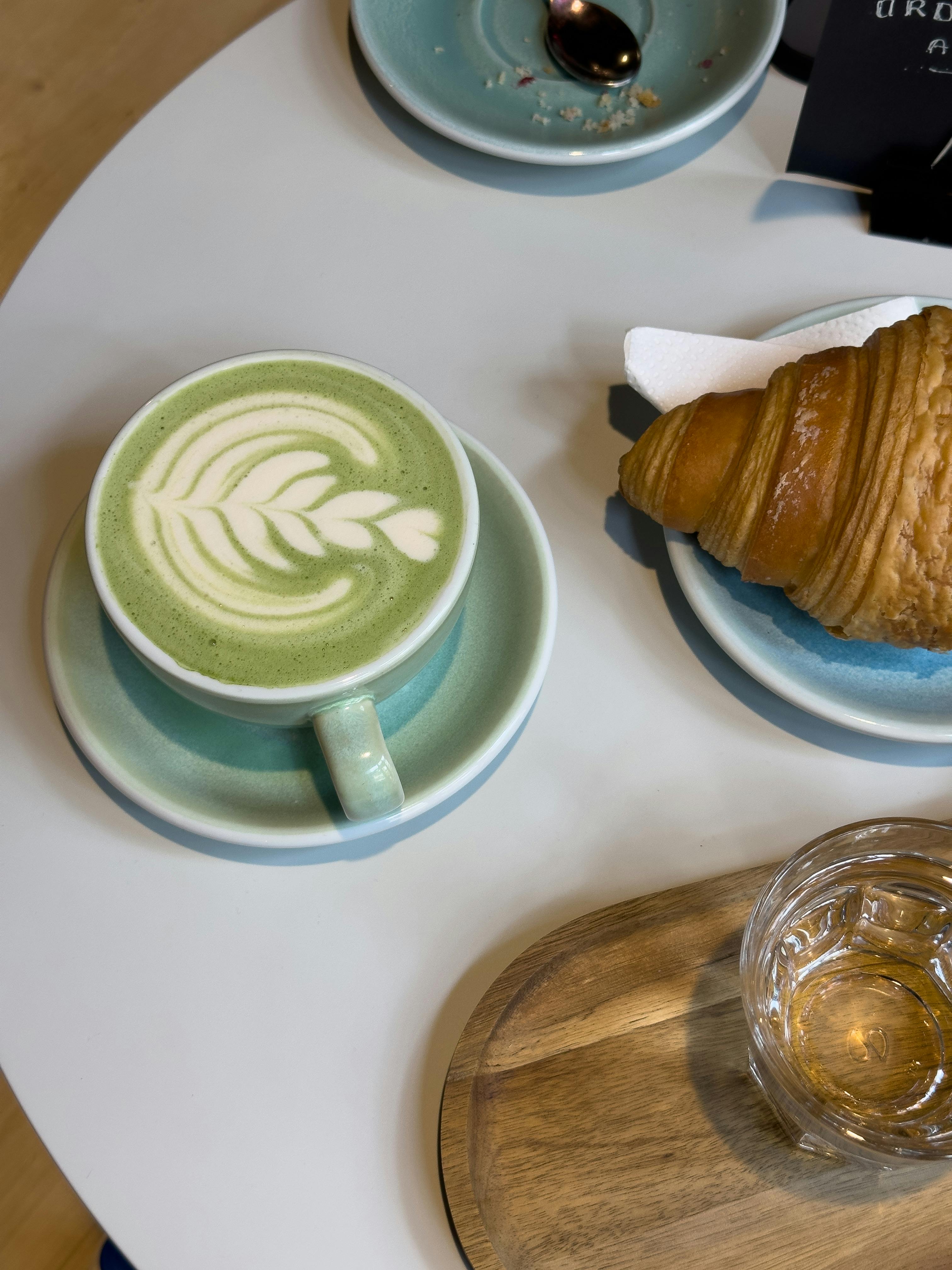 A cozy breakfast with a matcha latte and croissant on a cafe table.
