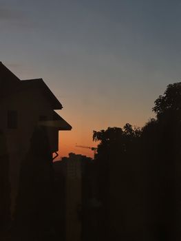 Silhouette of buildings and trees at sunset, urban landscape with crane.