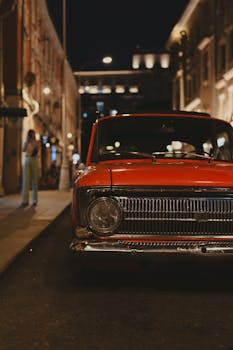 A classic red car parked on a dimly lit city street at night, capturing urban nostalgia.