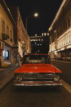 Classic red car parked under streetlights on an urban night scene.