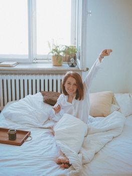 Woman stretching in bed, enjoying a calm and relaxing morning with soft daylight.
