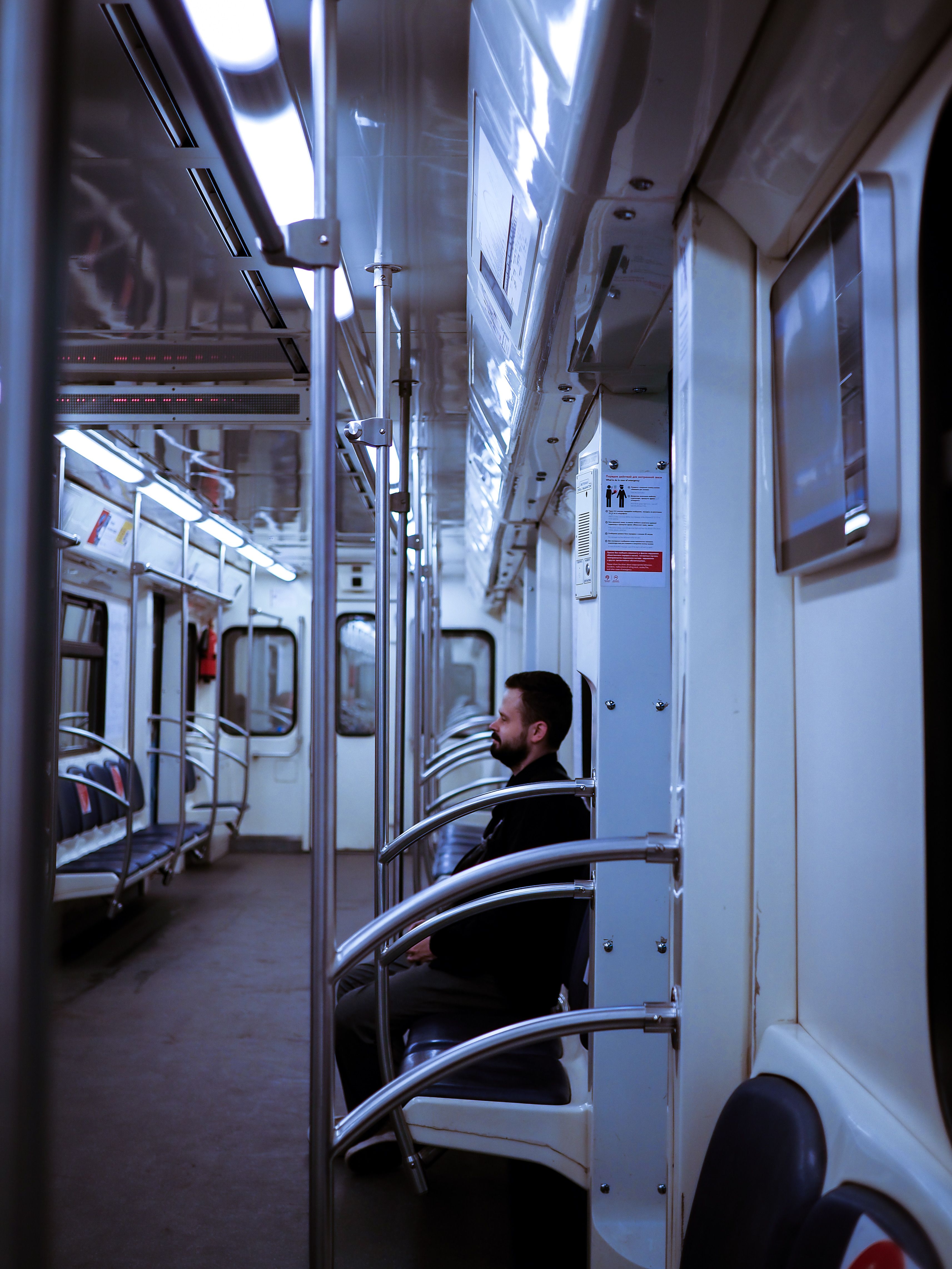 Free A man sits alone on a brightly lit, empty subway train, creating a serene and urban vibe. Stock Photo