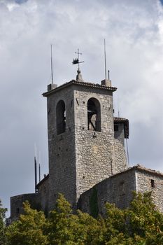 Historic tower of Guaita Fortress in San Marino, surrounded by greenery and under a cloudy sky.