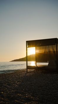 Stunning sunset on a pebble beach in Vlorë County, Albania, with a modern cabana.
