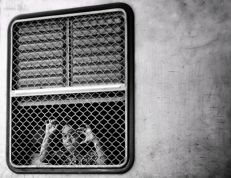 Black and white image of a child peering through a train window grate, capturing curiosity and introspection.