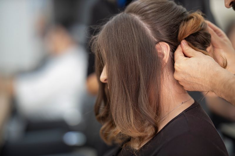Stylist finishing soft waves on a caramel balayage at the chair
