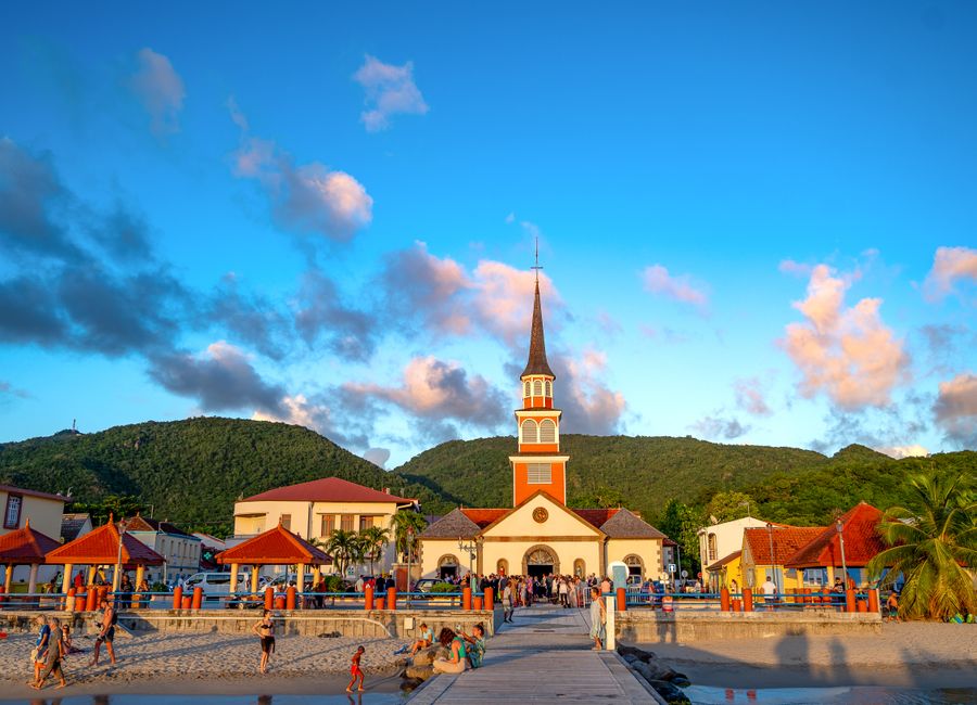 Vibrant tropical scene featuring a church, beach, and mountains during sunset.