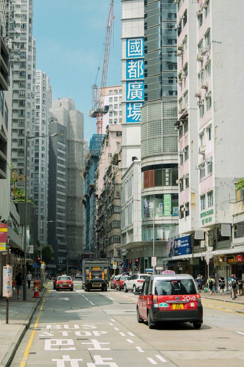 Free Vibrant Hong Kong street with taxis and skyscrapers on a sunny day, capturing city life. Stock Photo