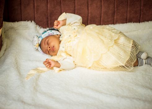 An adorable baby peacefully sleeping in a cream outfit on a fluffy white blanket.