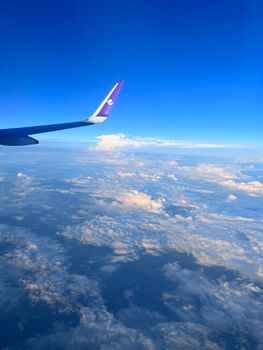 Aerial view from airplane with wingtip over fluffy clouds and blue sky. Perfect for travel and aviation themes.