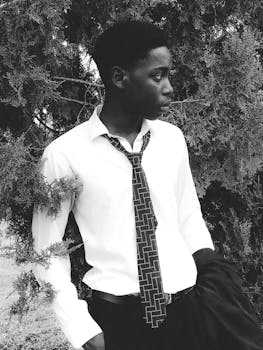 Black and white portrait of a young man in a tie outdoors, exuding confidence and elegance.