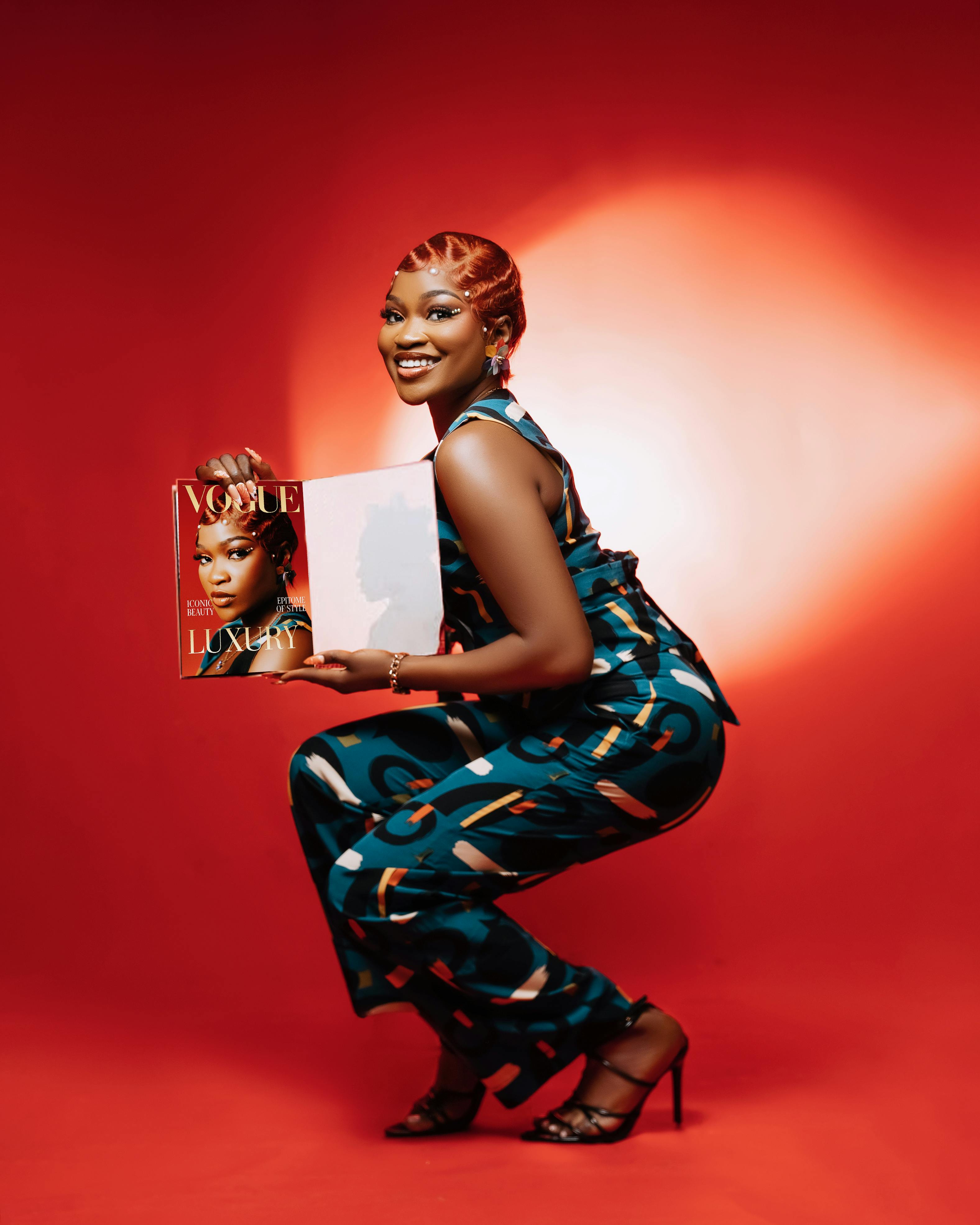 Fashionable woman in vibrant attire showcasing a magazine against a bold red backdrop.