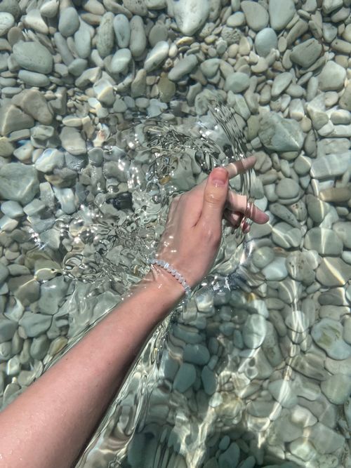 Free A tranquil moment with a hand in crystal clear water over pebbles, capturing summer vibes. Stock Photo