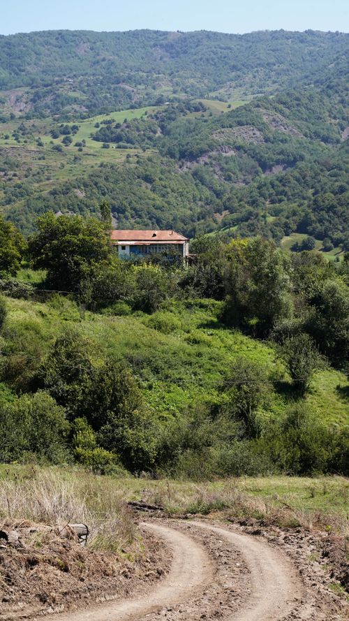 Free A peaceful country house nestled in vibrant, hilly green scenery under clear skies. Stock Photo
