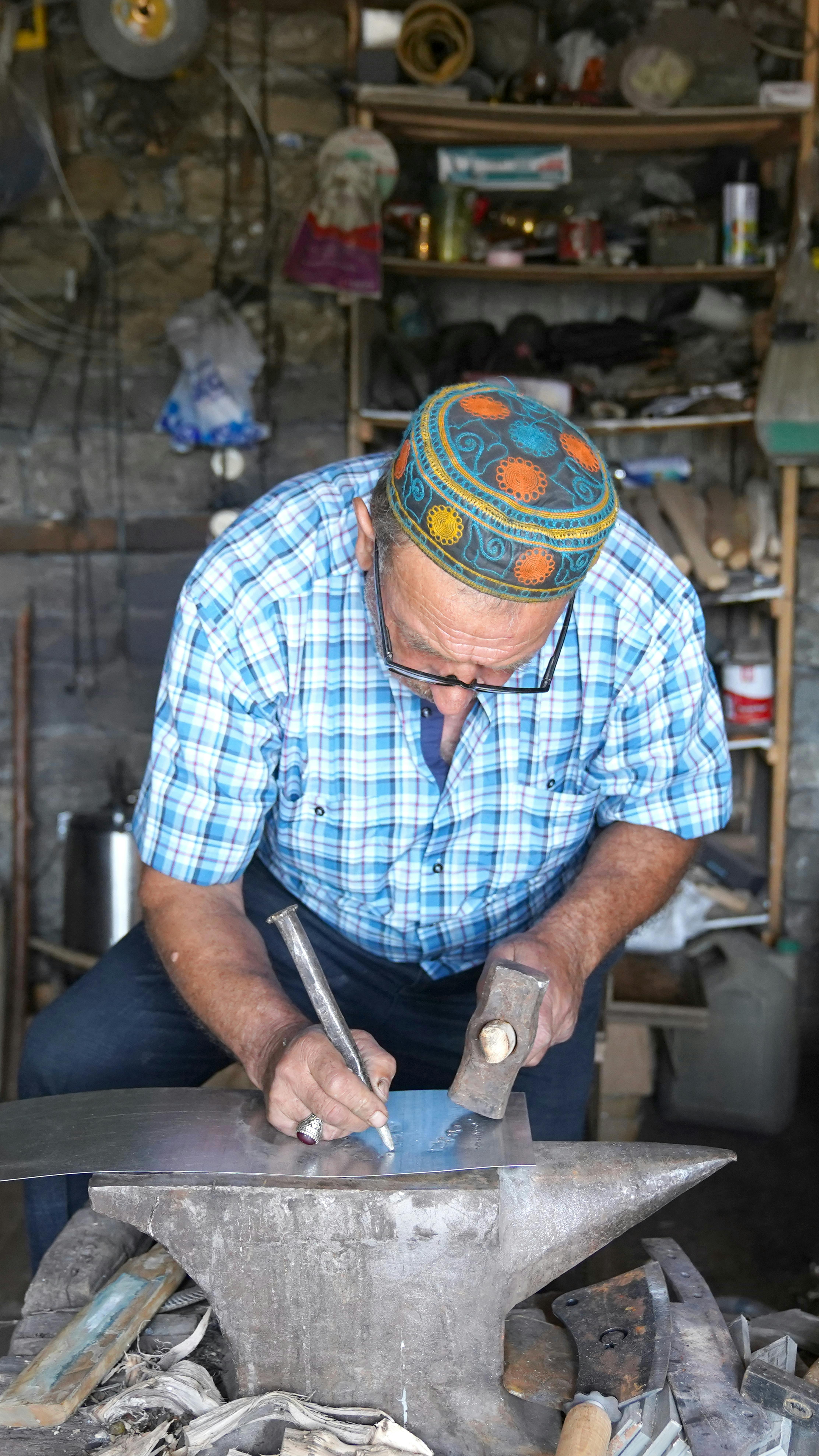 A skillful blacksmith engaging in traditional metalwork at an anvil inside a rustic workshop.