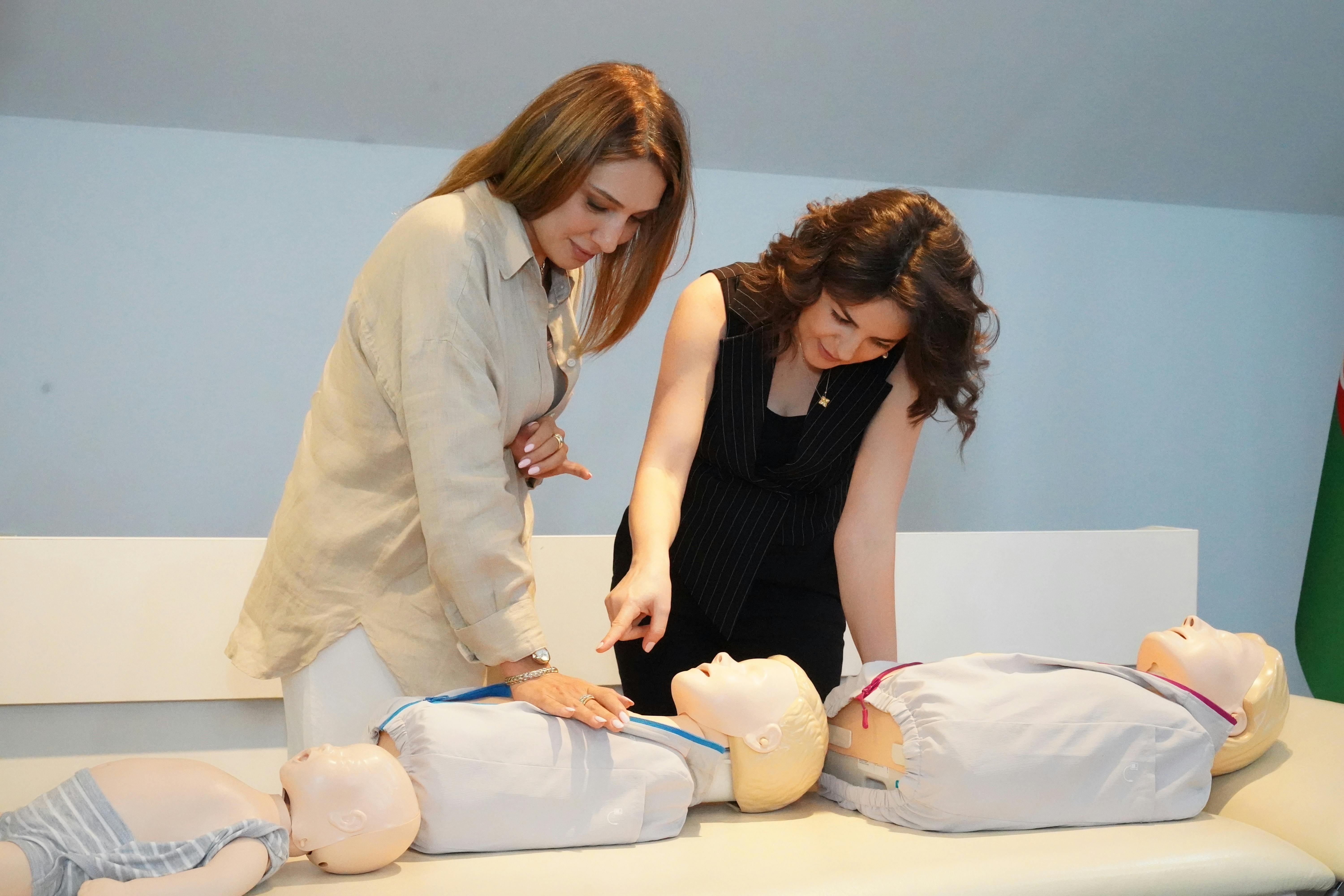Two women demonstrate CPR techniques on mannequins during a training session indoors.