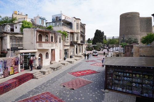 Free Traditional rugs displayed on a historic street with the Maiden Tower in view, capturing local culture. Stock Photo