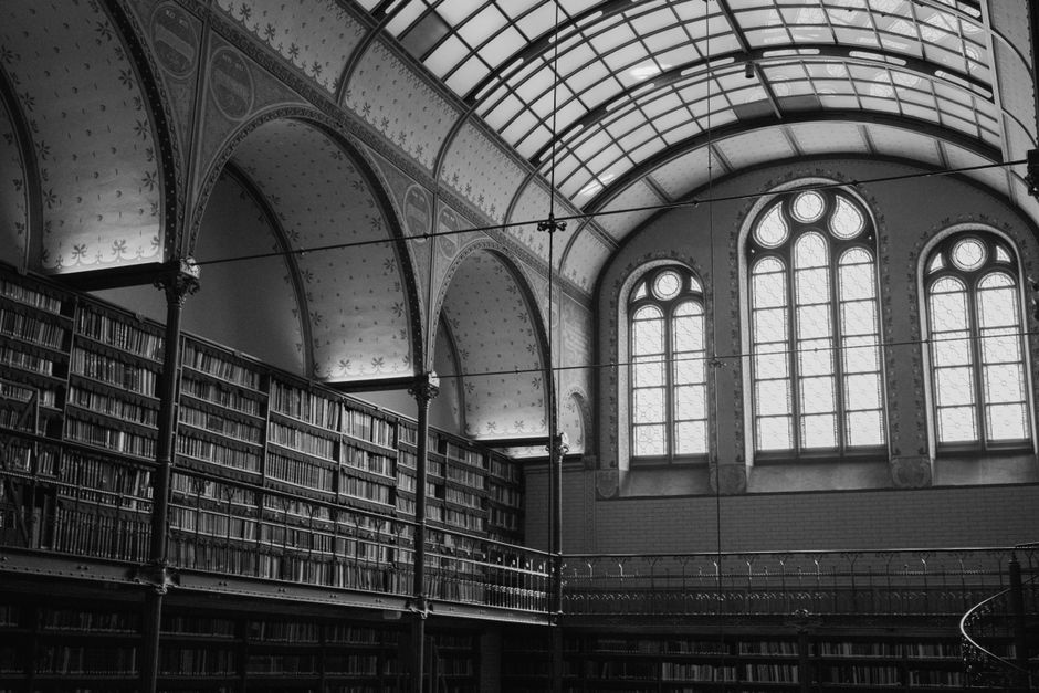 Black and white photo of a historic library in Amsterdam featuring arched windows and bookshelves.