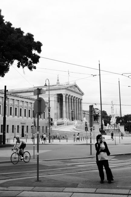 Black and white photo of a classical building with people and cyclist in an urban setting.