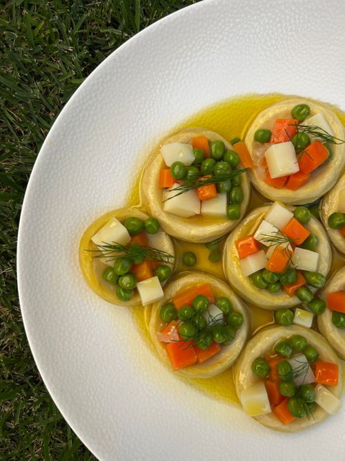 Free Fresh artichoke salad with peas and carrots on a white plate outdoors. Vibrant and healthy dish. Stock Photo