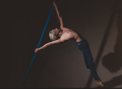 Free A muscular man performs a graceful pole dance move in dimly lit studio, showcasing strength and flexibility. Stock Photo