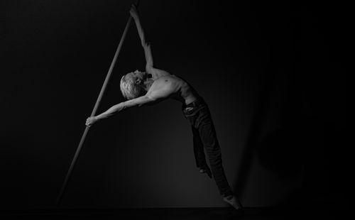 Free A man performing a dramatic dance move with a pole in a black and white studio setting. Stock Photo
