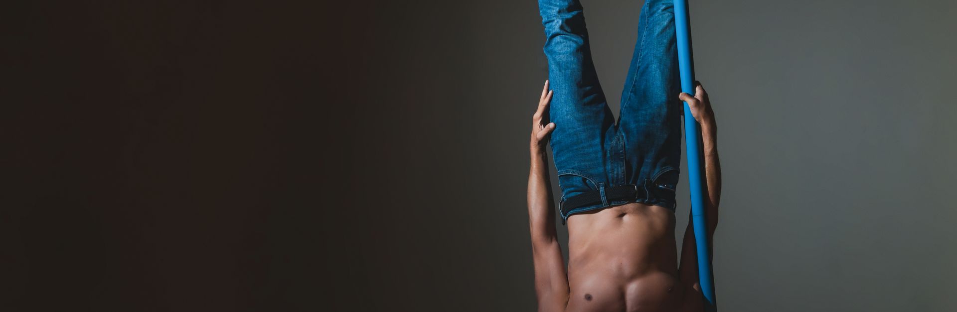 Athletic adult performing an acrobatic pole stunt, hanging upside down.