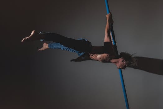 A male athlete showcasing strength and skill while performing on a pole in a studio setting.