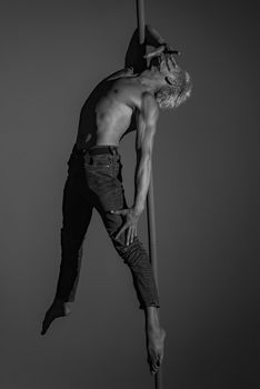 A striking black and white image of a shirtless man performing pole dance, showcasing strength and grace.