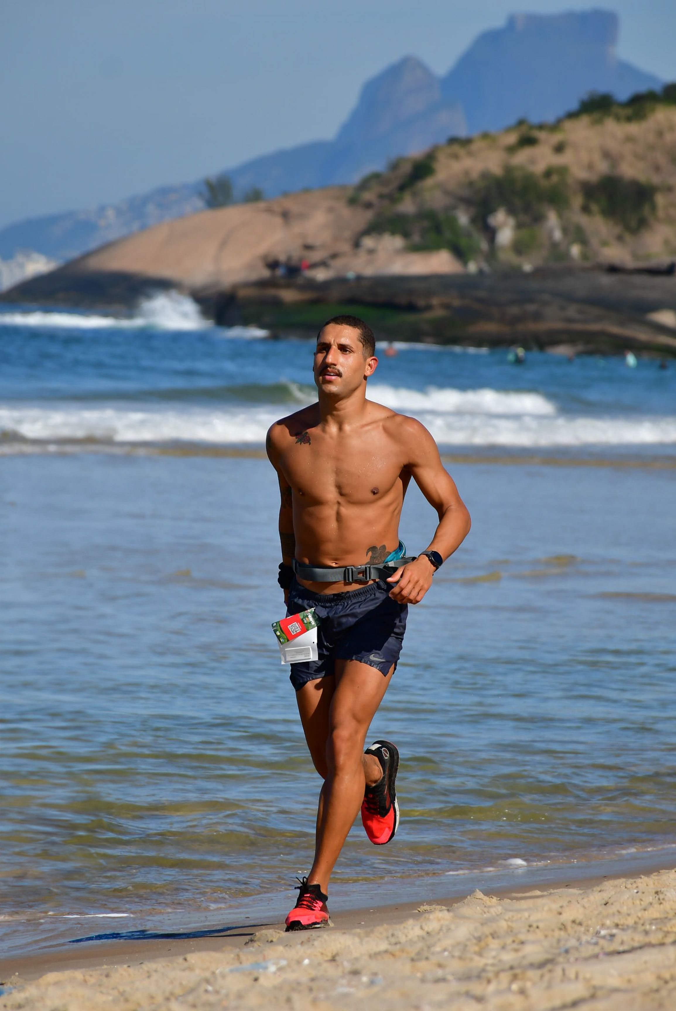 A fit man jogs on the sandy beach in Niterói, Rio de Janeiro, with scenic coastal views.