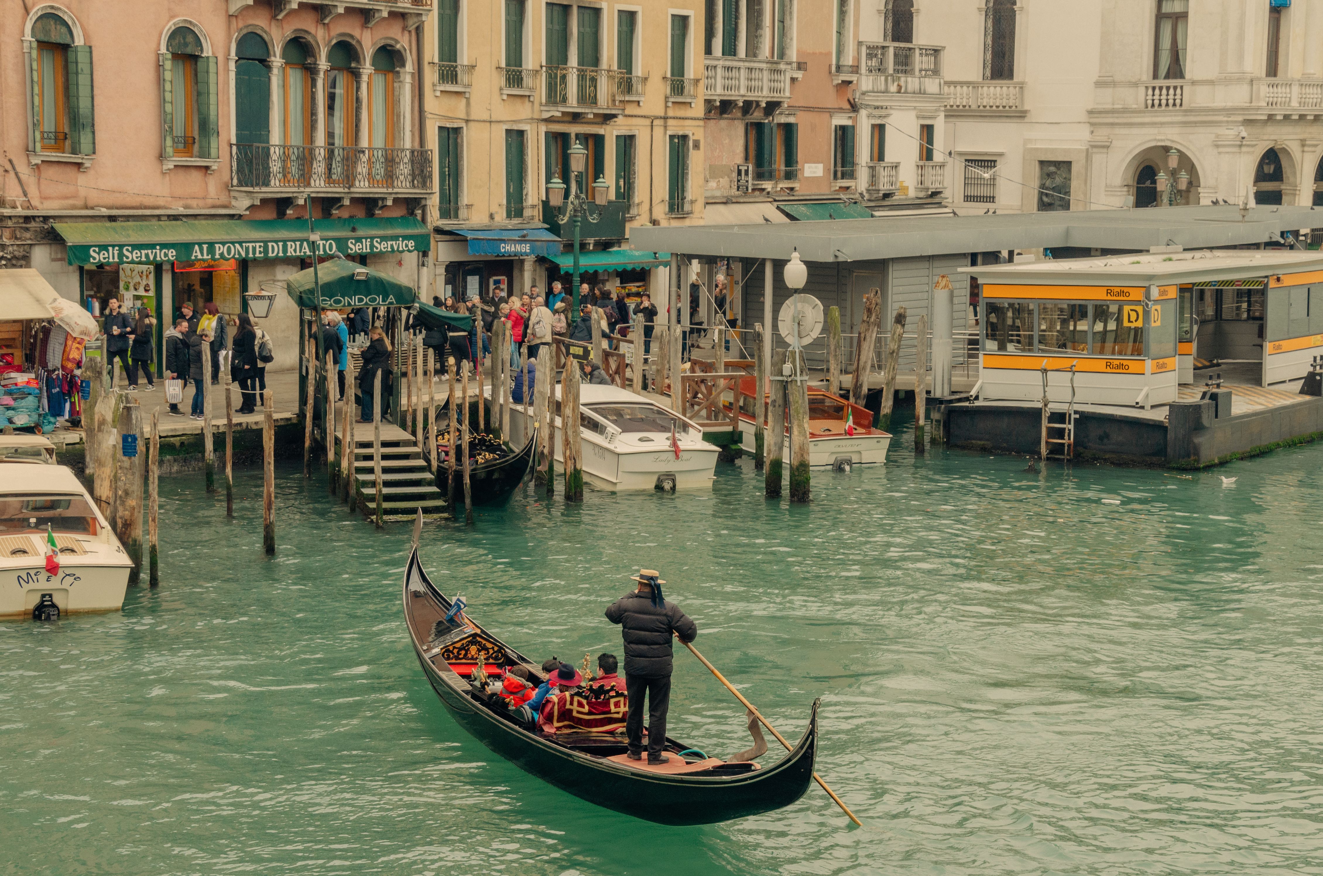 A gondolier maneuvers his gondola along a bustling Venice canal near Rialto Bridge.
