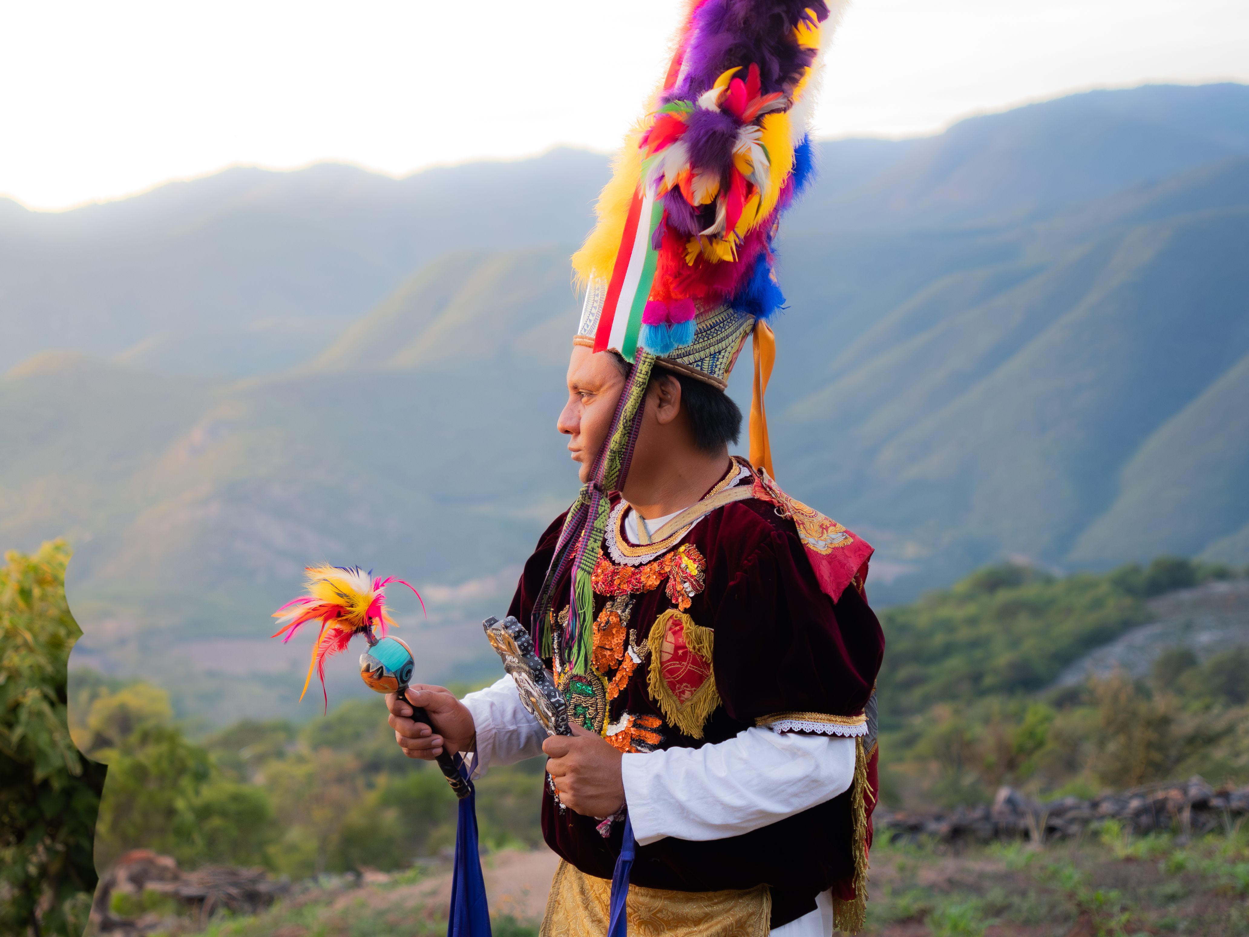 A vibrant traditional dancer in Oaxaca, Mexico with colorful attire against a mountainous backdrop.