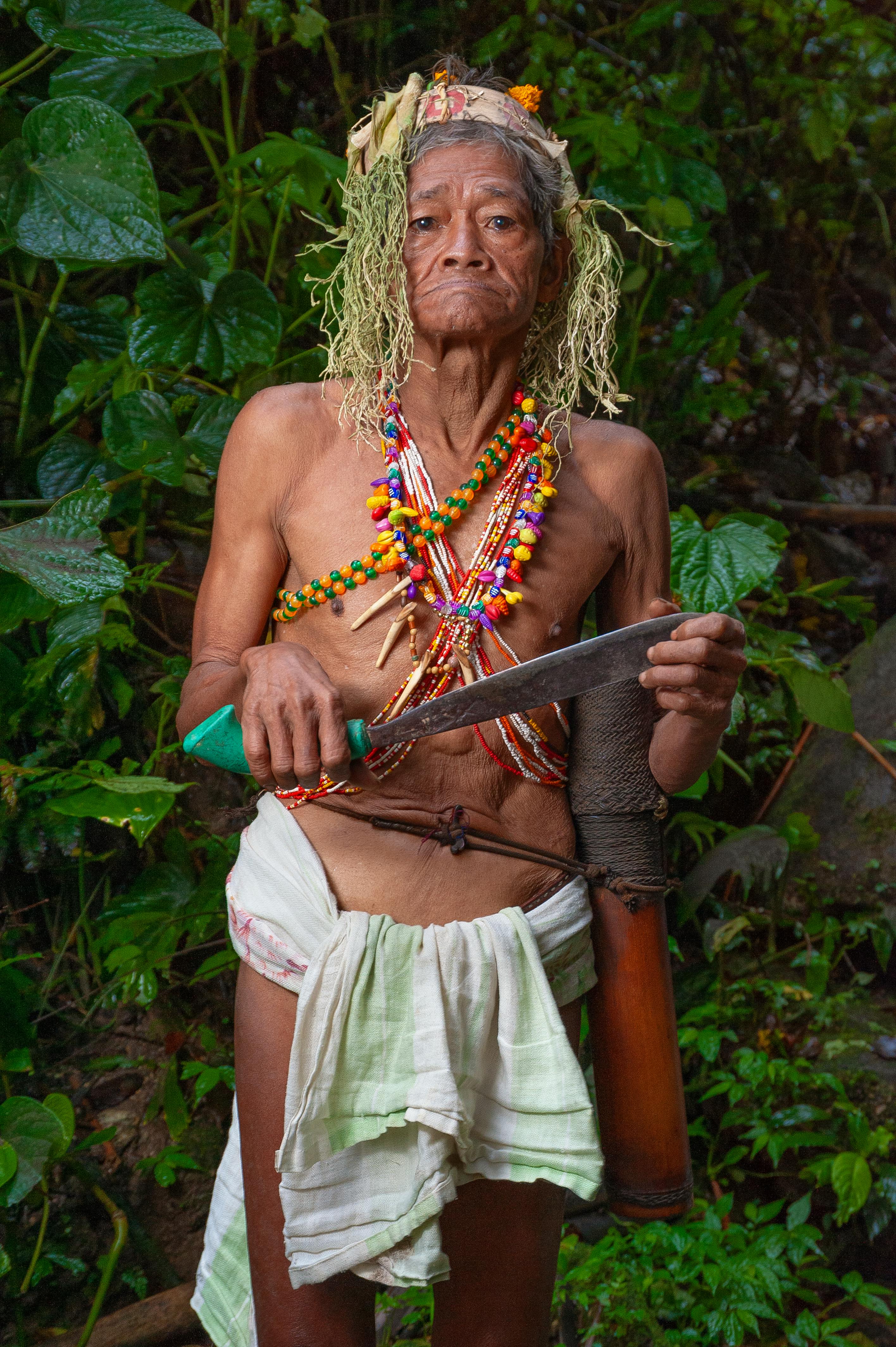 Elderly indigenous man with traditional attire in Malaysian rainforest setting.