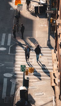 Aerial view of pedestrians crossing a street in an urban setting during day with long shadows.