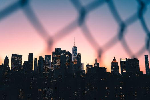 Captivating view of New York City skyline at sunset framed by a chain-link fence.