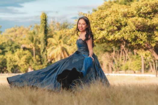 Elegant portrait of a young woman in a blue dress posing gracefully in a sunny meadow.