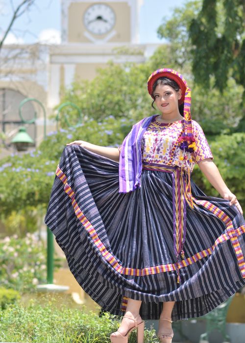 Free Woman in vibrant traditional Mexican attire posing cheerfully in a sunny outdoor plaza. Stock Photo