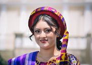 A woman smiling outdoors in vibrant traditional clothing with intricate patterns.