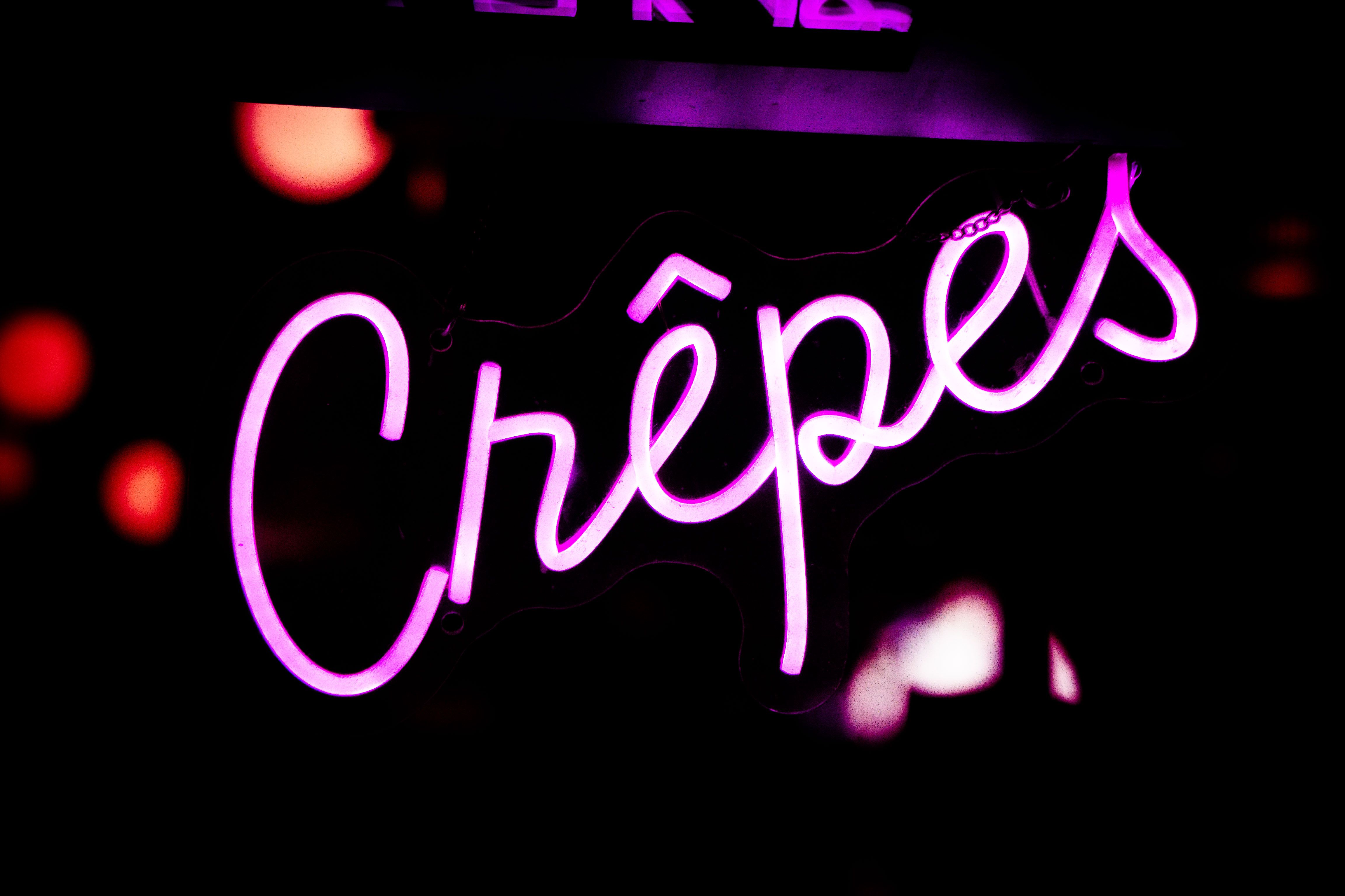 Eye-catching neon crêpes sign glowing in purple and pink lights, Paris ambiance.