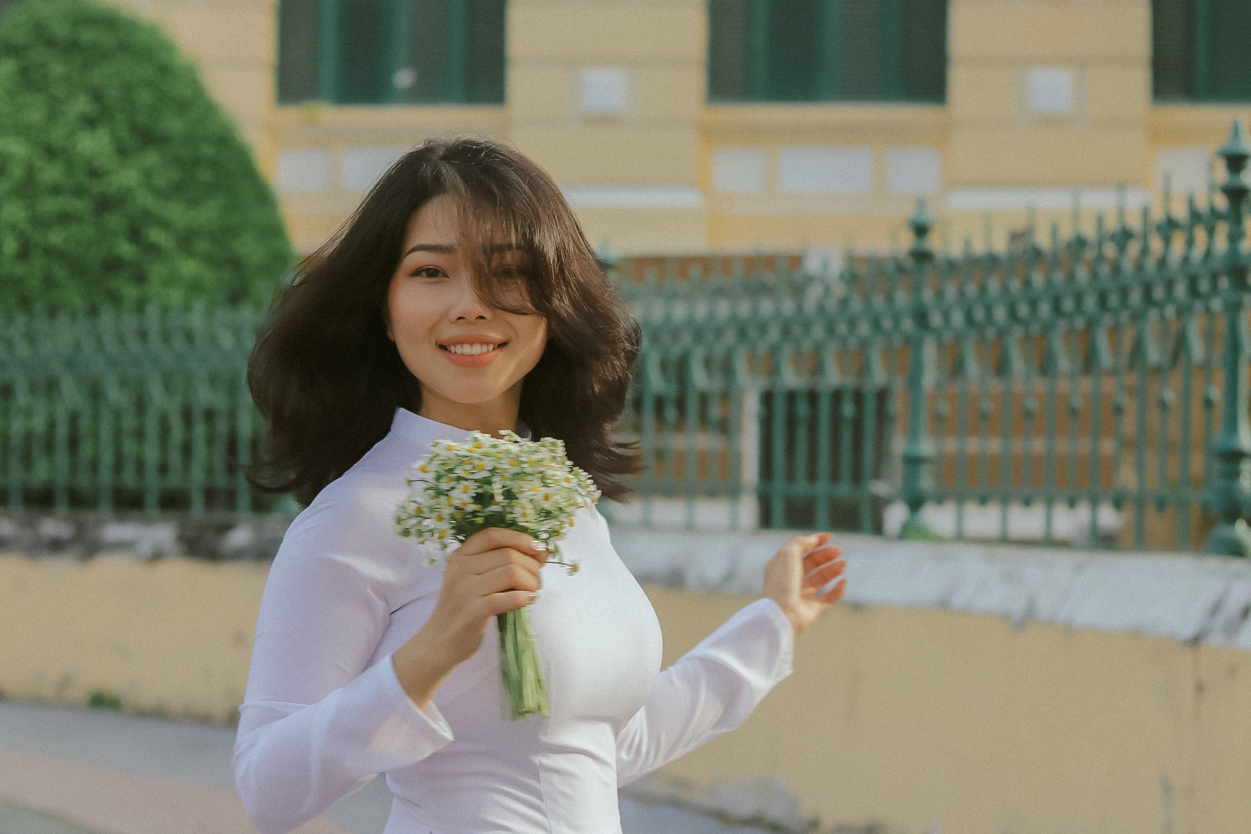 Smiling woman in traditional Ao Dai holding flowers outdoors in Ho Chi Minh City, Vietnam.