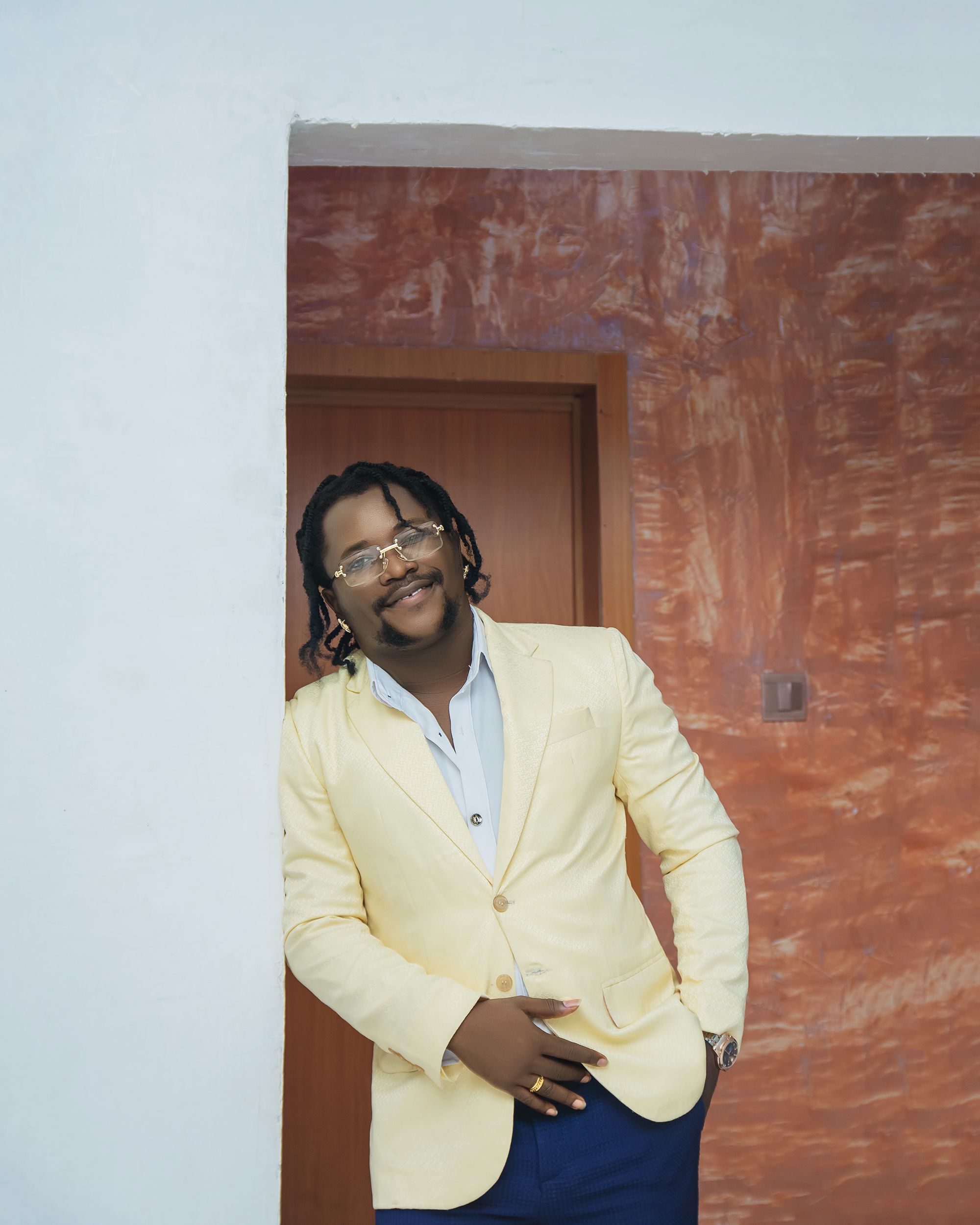 Elegant man in a yellow suit leaning against wall indoors with smile.