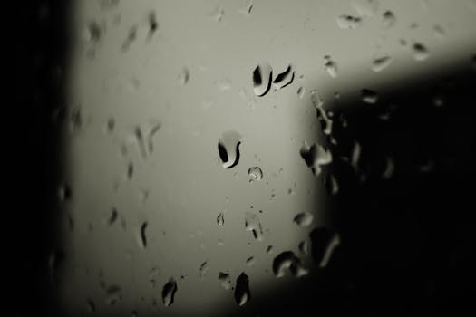 Close-up abstract view of raindrops on a glass window creates a moody ambiance.