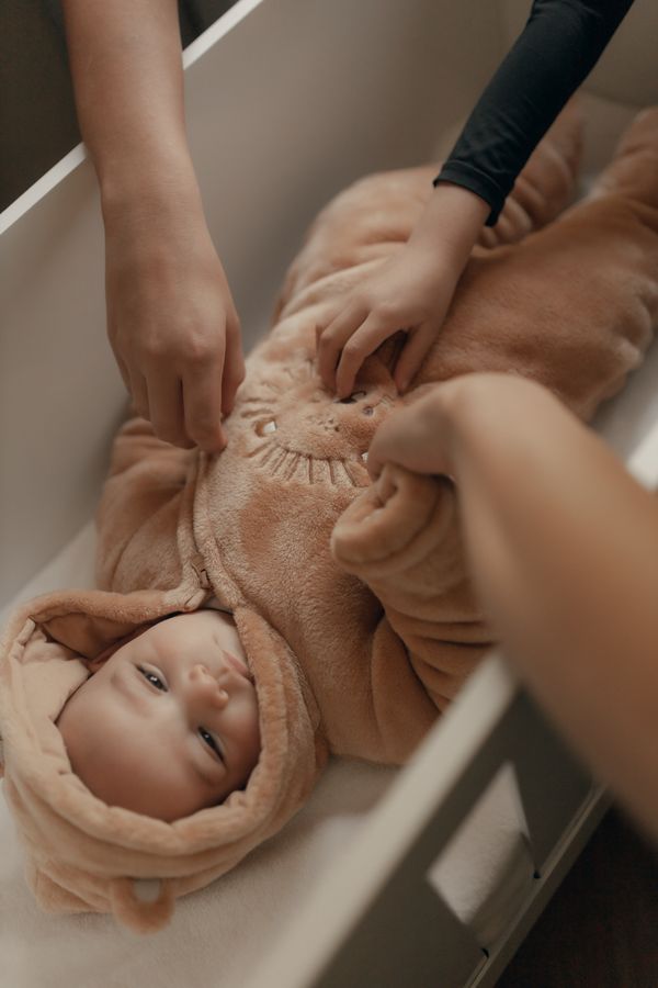 parent zipping baby into a cozy hooded winter sleeper in a crib at bedtime