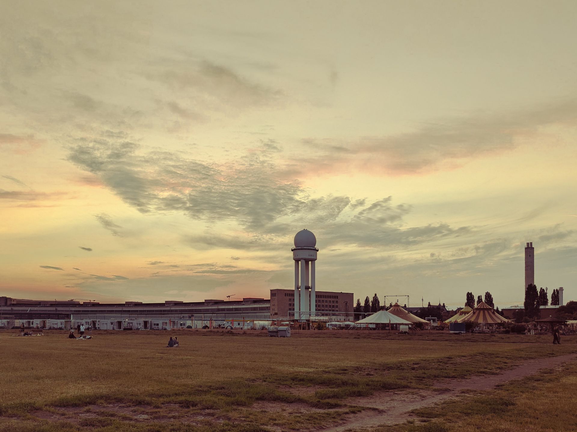A peaceful summer sunset over Tempelhofer Feld in Berlin, with a radar tower and tents in the distance.