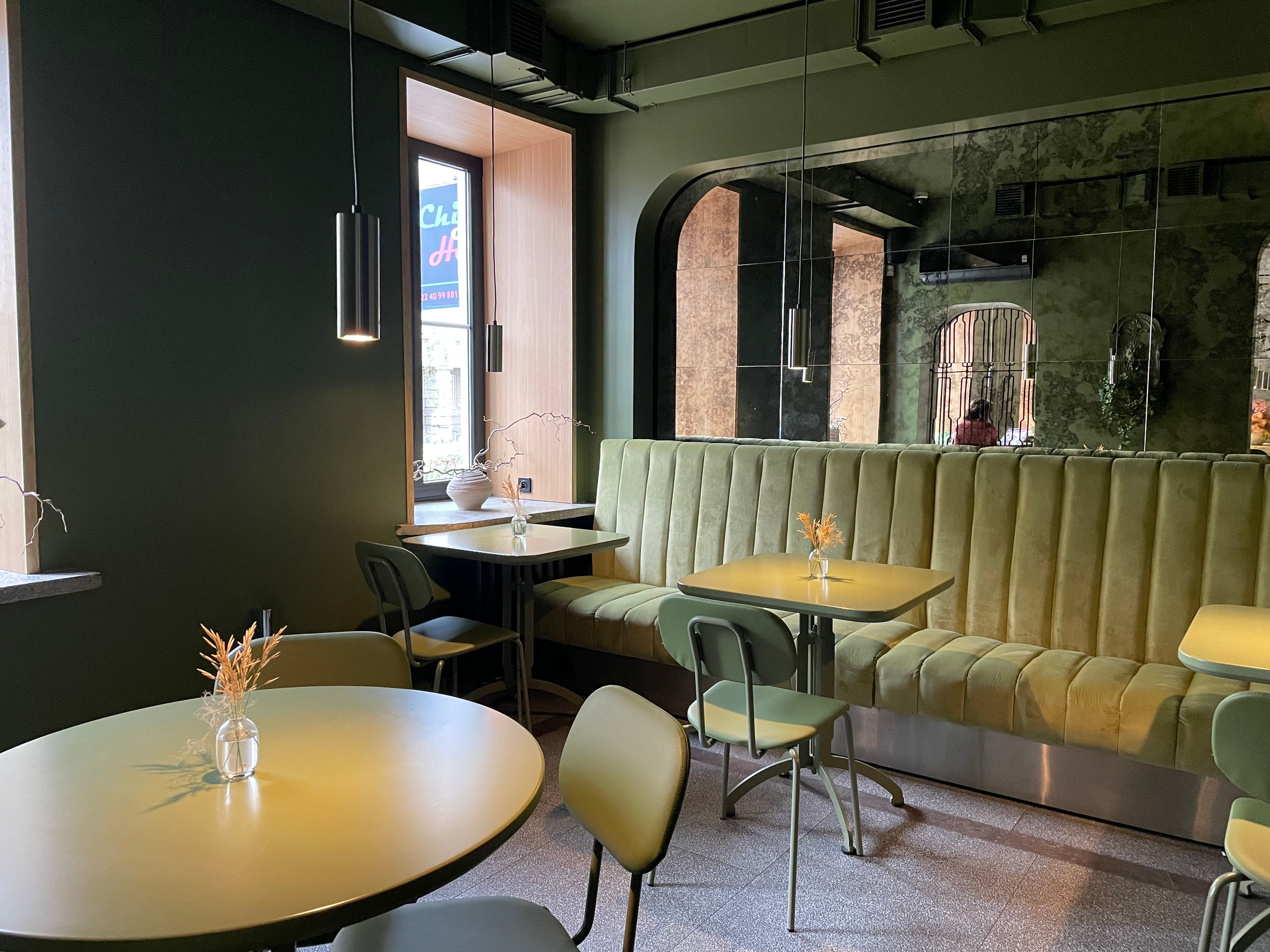 Chic cafe interior in Warsaw featuring green velvet seating and minimalist decor.